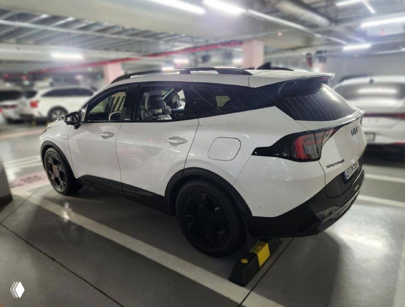 Задний и боковой вид белого KIA Sportage 2025 в подземной парковке, заметны задние фонари, форма крыши и общий профиль кроссовера.