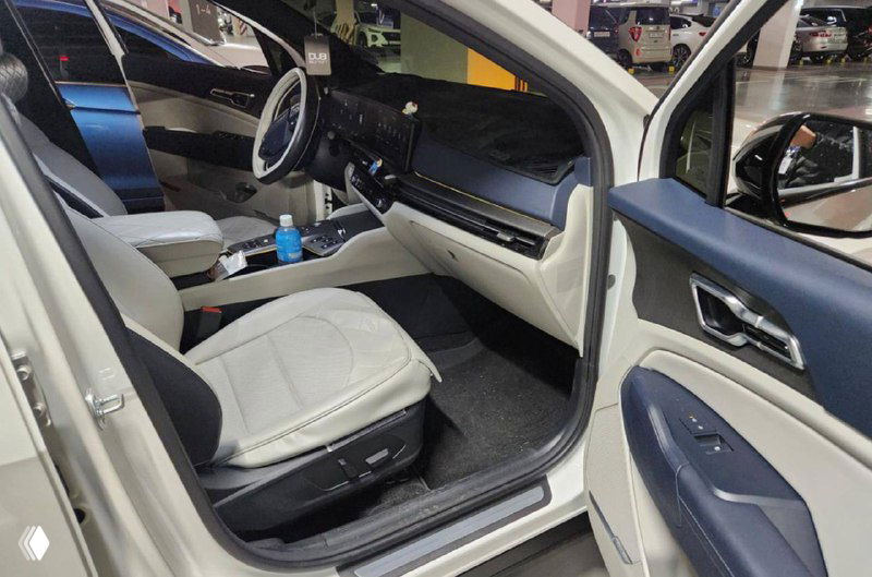 Переднее пассажирское сиденье и часть салона KIA Sportage 2025 с бежевой обивкой, открытая дверь и вид на отделку дверной панели и порог.