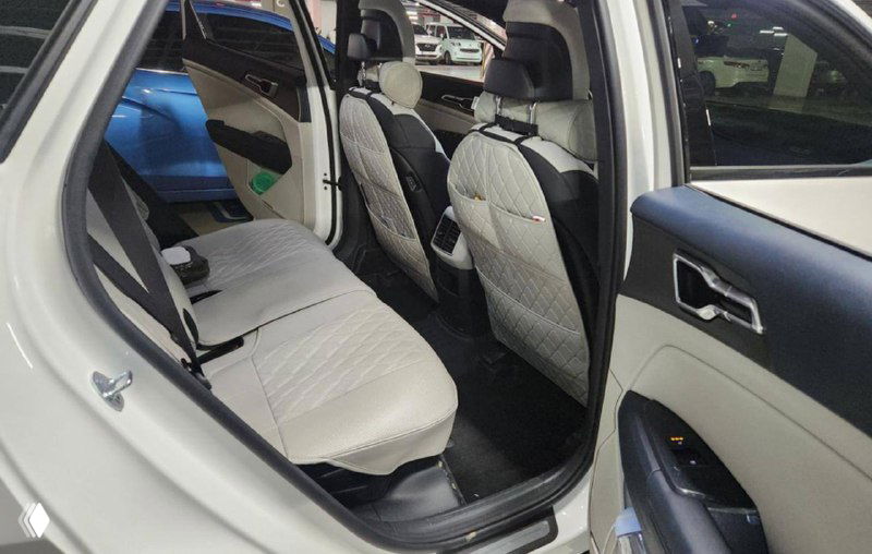 Задний ряд сидений KIA Sportage 2025 с бежевой обивкой, видно пространство для ног, спинки и дверную панель с ручкой и карманом.