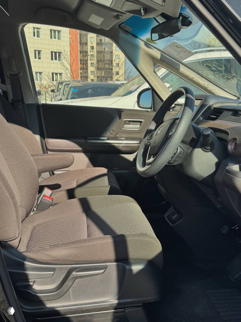 Водительское сиденье и пространство передней части салона Honda Freed 2021: тканевая обивка, подлокотник и обзор из кабины видны на фото.