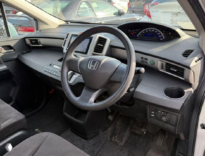 Салон Honda Freed: вид на рулевое колесо, панель приборов и переднюю часть салона, отчётливо видны приборная панель, консоль и состояние обивки.