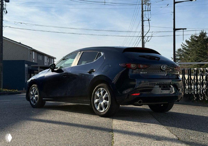 Задний ракурс тёмно‑синей Mazda 3 BP5P 2021 года на площадке в Японии, видна форма фонарей, крышка багажника и общий силуэт автомобиля на фоне деревьев.