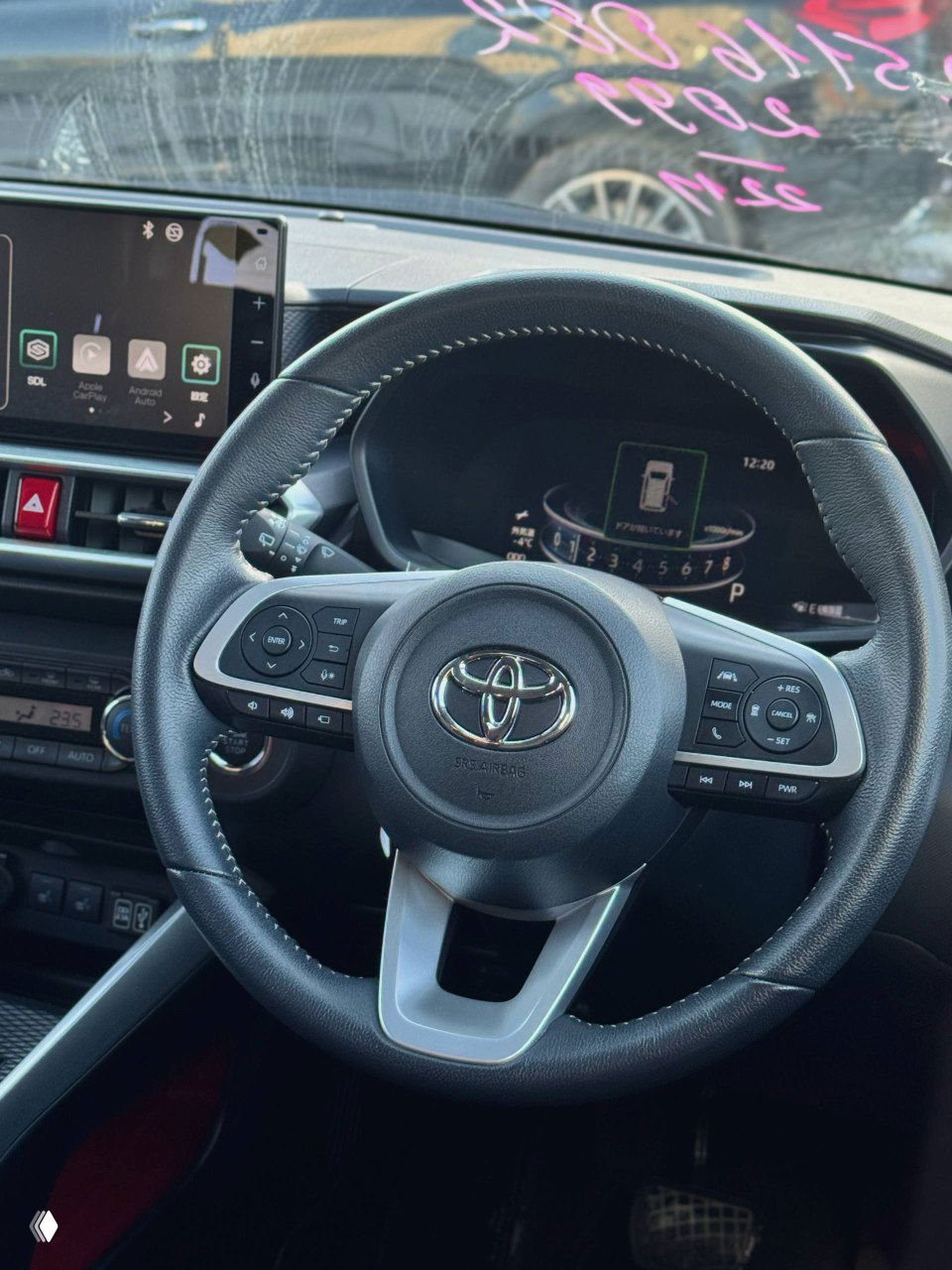 Руль Toyota с мультикнопками, панель приборов и часть лобового стекла видны крупным планом; рулевое колесо в хорошем состоянии.