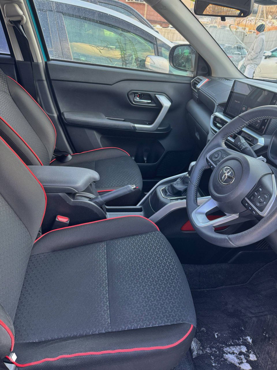 Передние сиденья и центральный тоннель Toyota Raize, чёрная обивка с красной прострочкой, общий вид переднего салона и подлокотник.