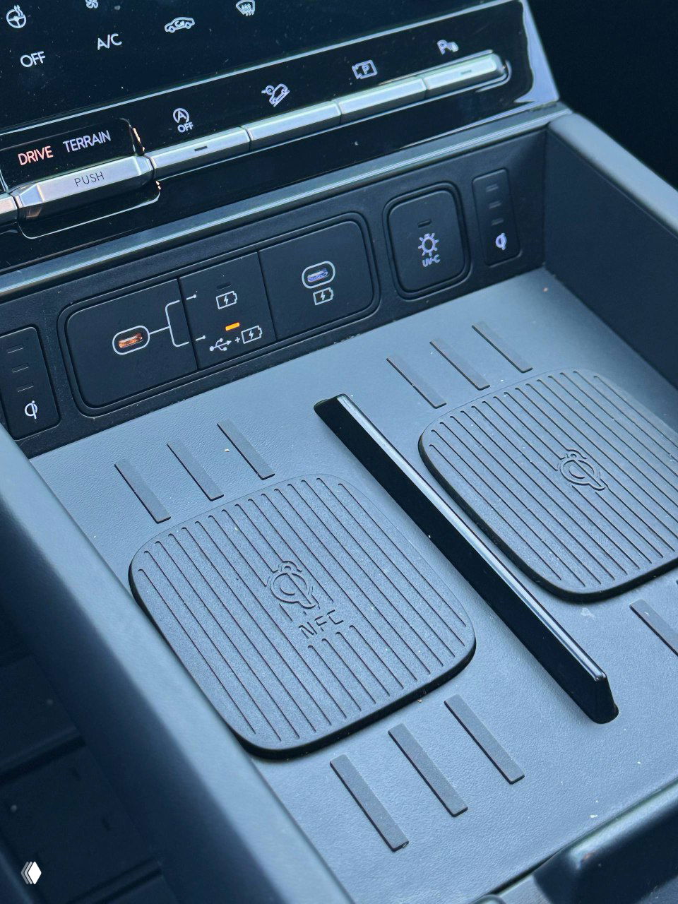 Зона между передними сиденьями с беспроводными зарядками NFC и несколькими USB-портами, панель управления вспомогательными функциями в центре салона.