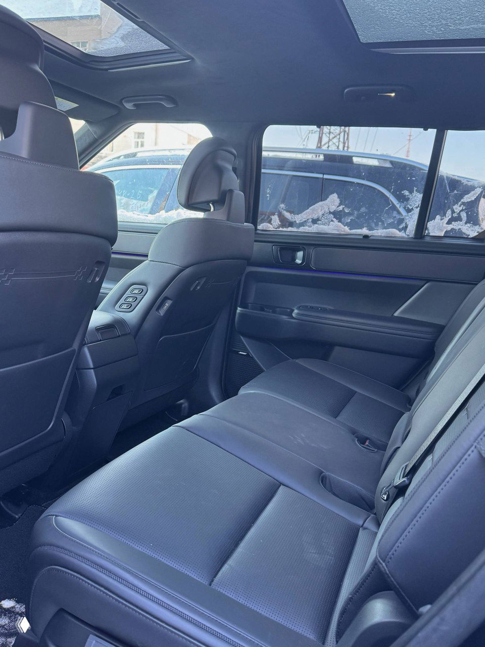 Задний ряд сидений Hyundai Santa Fe с кожаной обивкой, вид на простор салона и задние подлокотники, фото сделано при дневном освещении на стоянке.