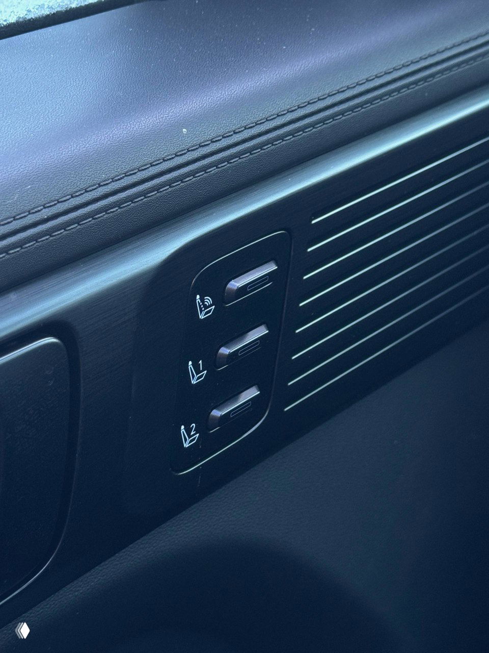Крупный план блока регулировок на двери с пиктограммами функций сидений и вентиляции, чёрная отделка и декоративные вставки рядом с ручкой.