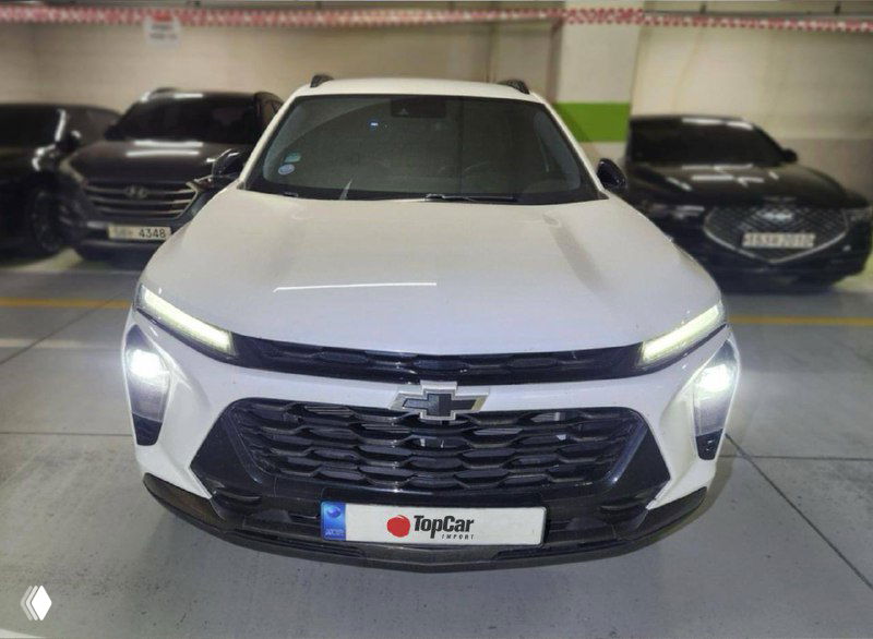 Белый Chevrolet Trax — вид спереди в подземном паркинге, включённые фары и табличка TopCar; фото экстерьера для объявления о продаже.