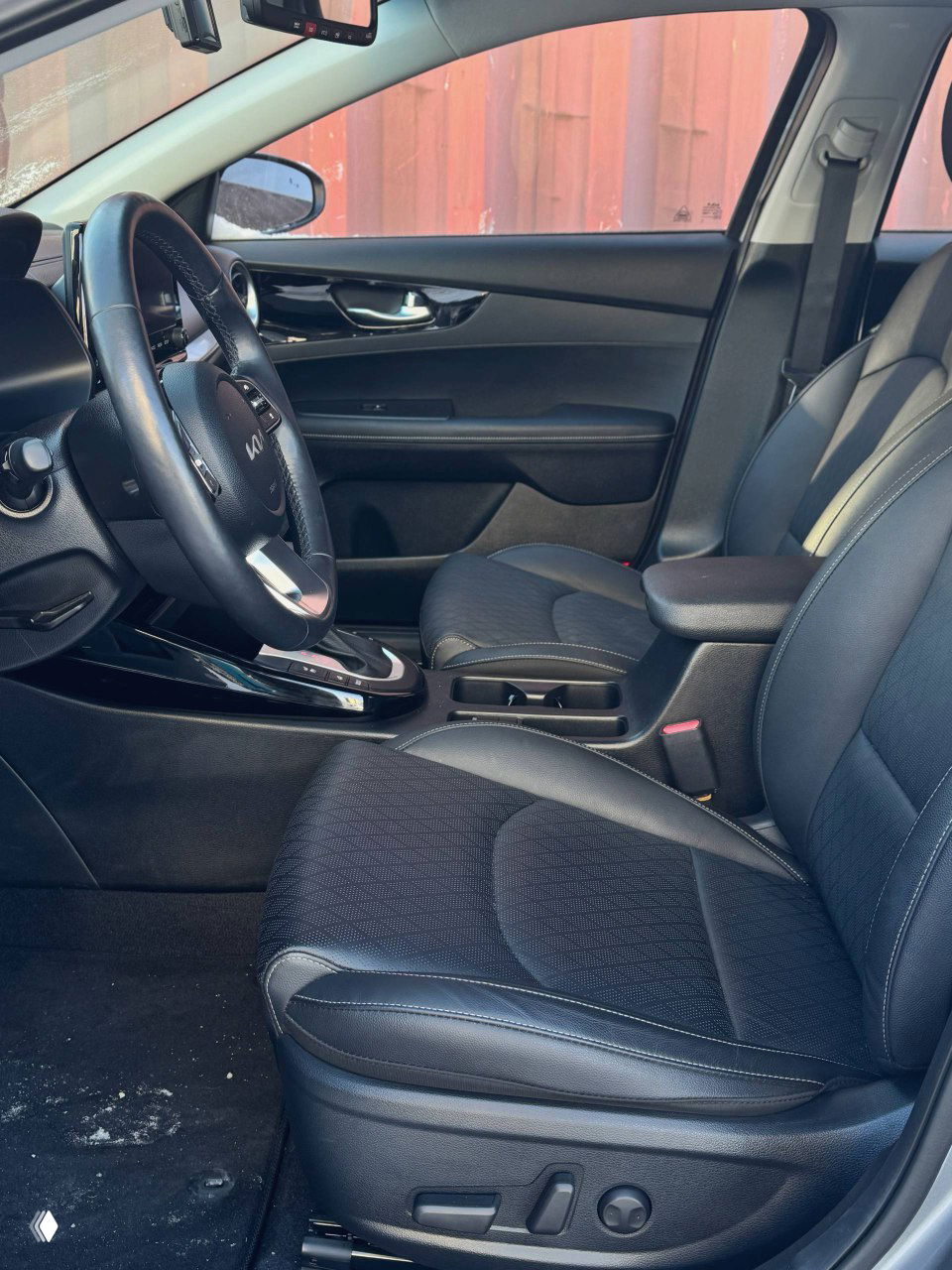 Вид салона KIA K3: передние кресла, центральный подлокотник и обзор по дверям; тёмная обивка и аккуратная прострочка.
