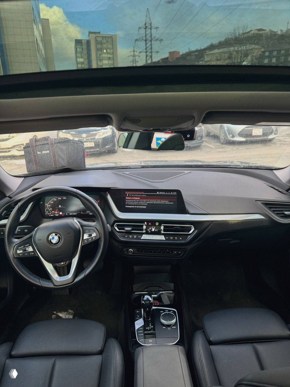 Панорамный вид салона BMW 220i: передняя панель, мультиинформационный экран и руль, вид на парковку через лобовое стекло в зимних условиях.