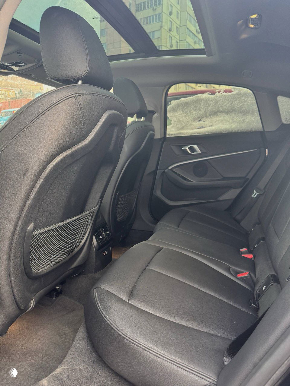 Задний ряд сидений BMW 220i: кожаные сидения, простое пространство для ног и дверные панели, вид с угла на второй ряд салона и панорамную крышу.