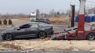 Тёмный седан на рампе автовоза во время погрузки, вид с обочины — фрагмент видео перед отправкой в порт Пусан.
