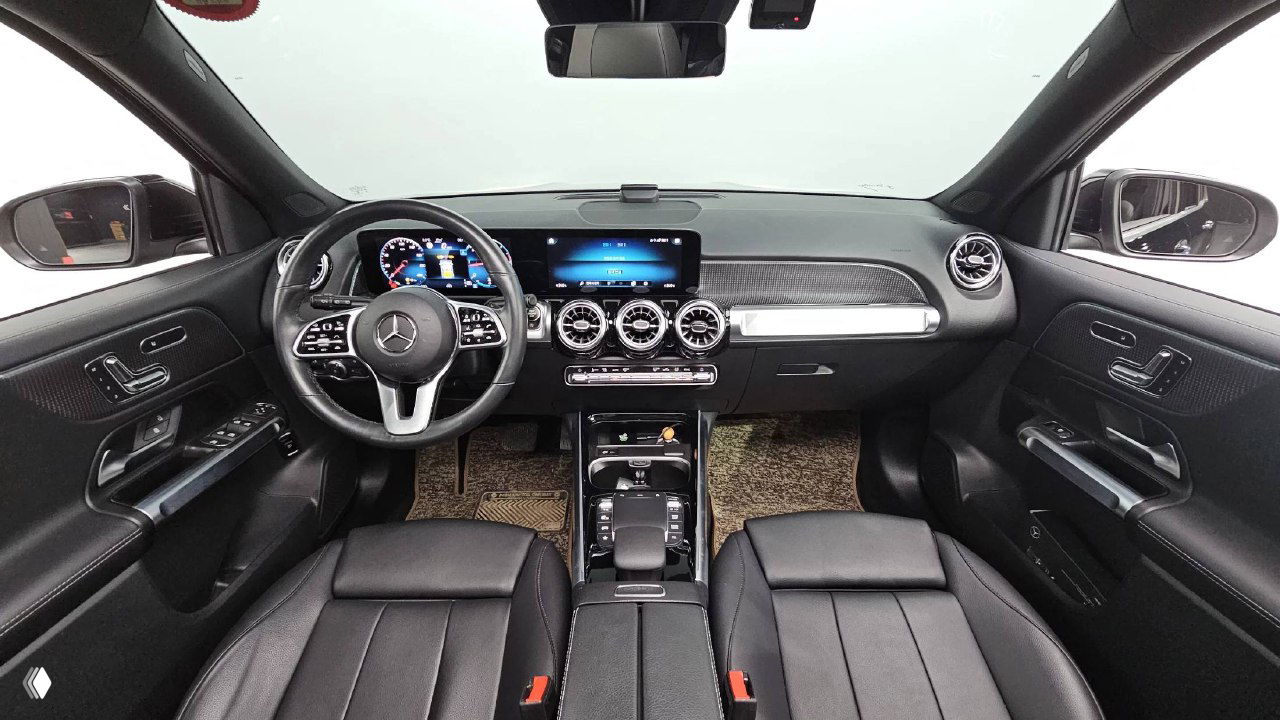 Салон Mercedes GLB200d: передняя часть, мультимедийный экран и цифровая приборная панель, руль и передние кожаные сиденья чёрного цвета.