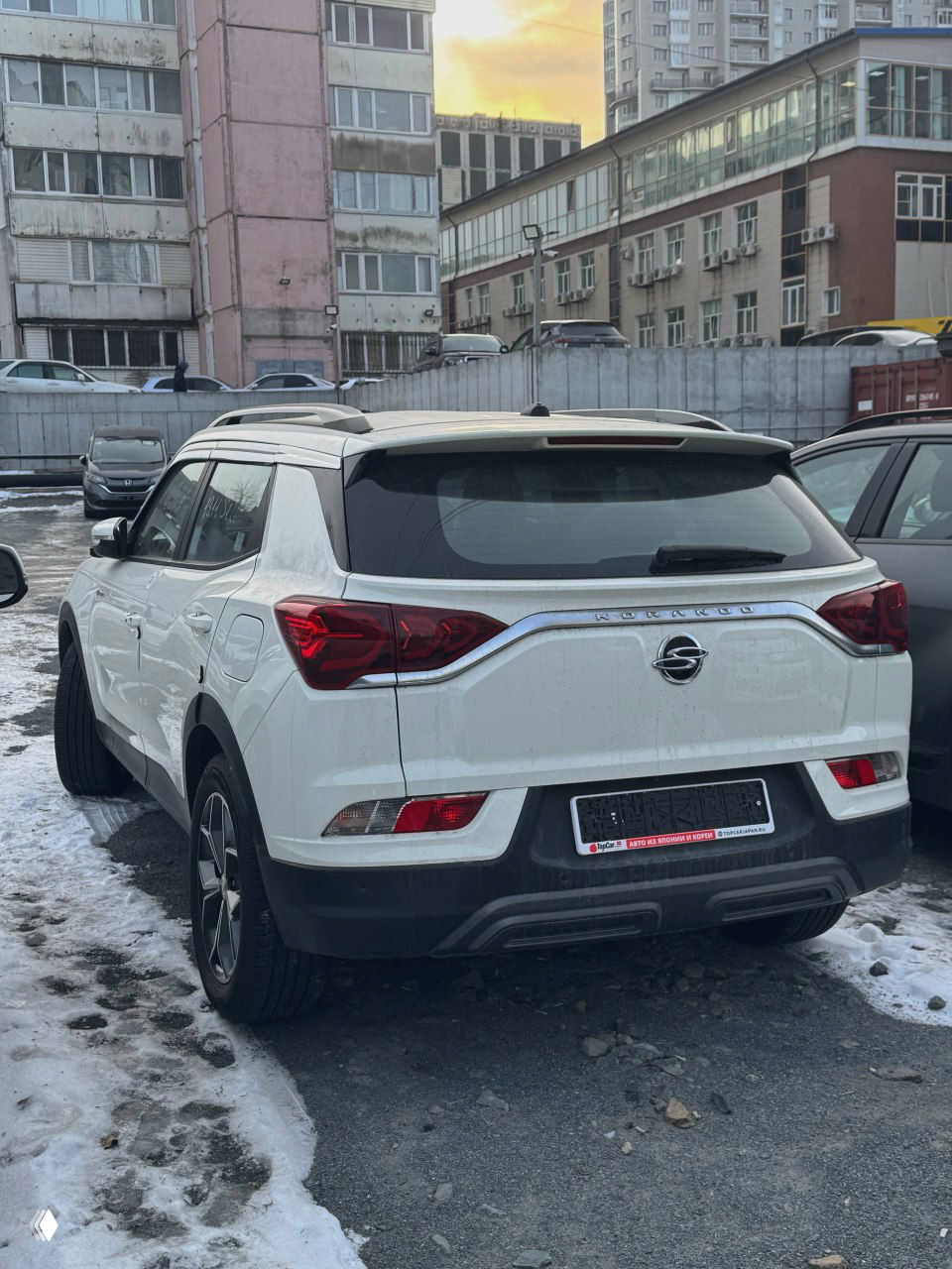 Задняя часть белого SsangYong Korando 2021 — вид сзади‑слэва, багажник, задние фонари и задний бампер на городском фоне с сугробами.