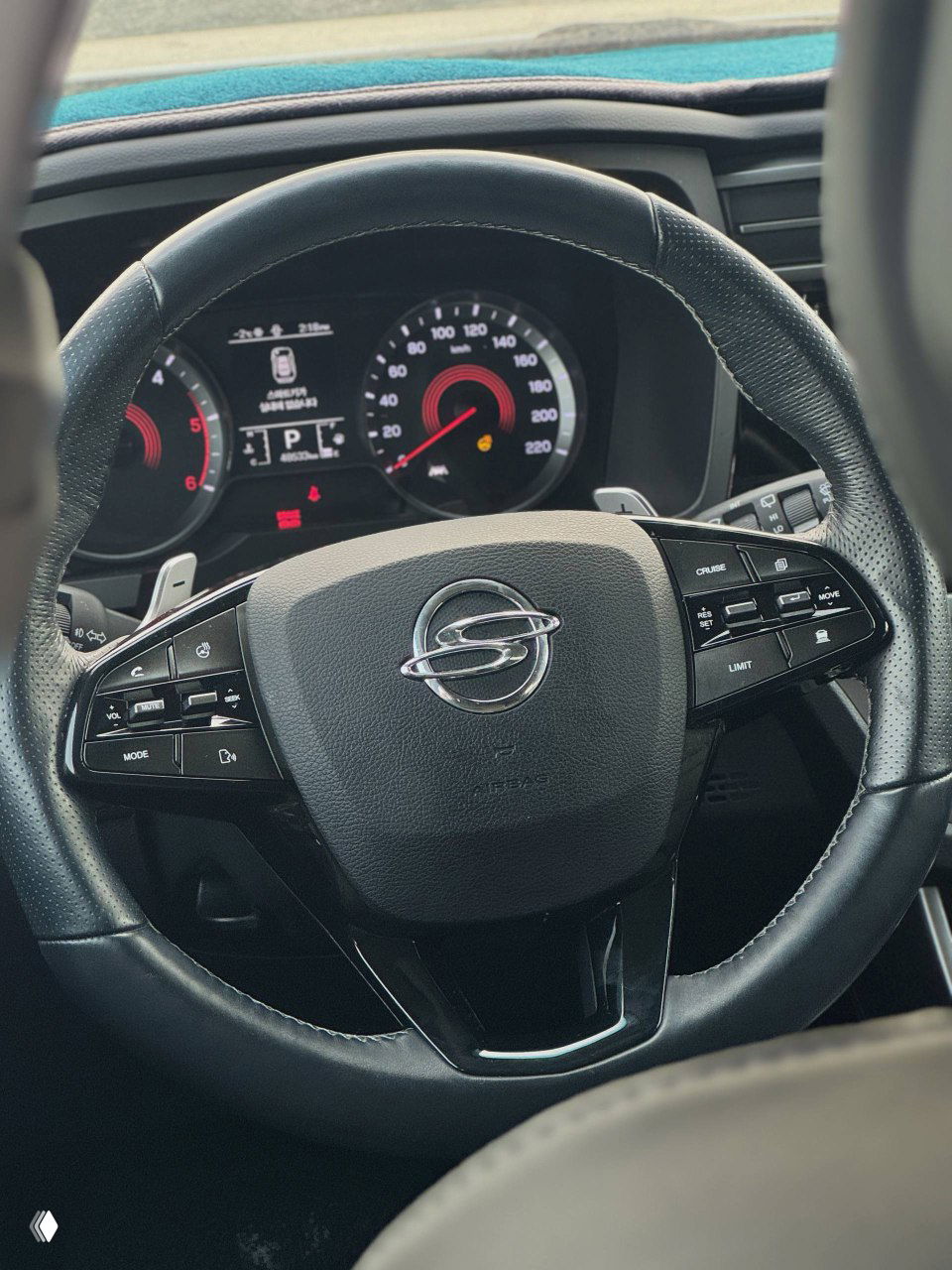 Рулевое колесо SsangYong Korando с логотипом на центральной подушке, крупный план приборной панели и элементов управления на руле.