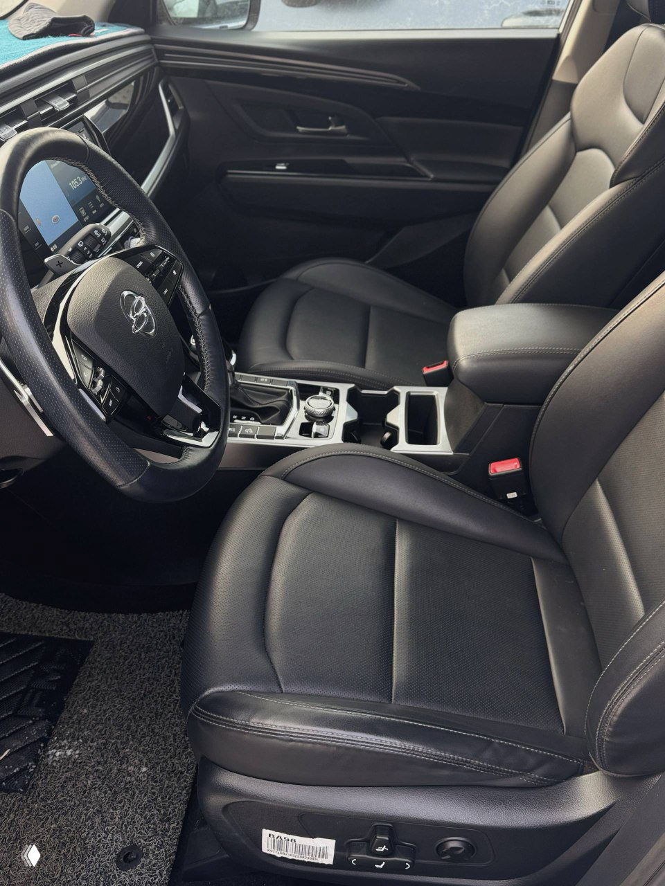 Передние сиденья и центральный подлокотник белого SsangYong Korando, чёрная кожаная обивка и вид на центральный тоннель с подстаканниками.