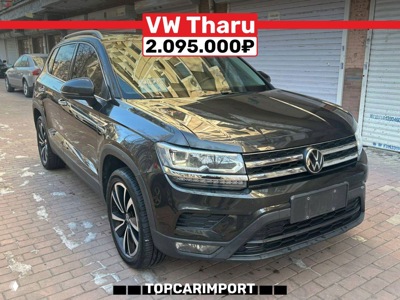 Фотография Volkswagen Tharu (2021) на улице — вид спереди, тёмный кузов, запас дорожного пространства и цена 2.095.000₽ на баннере.