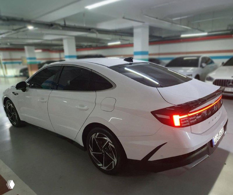 Задняя часть белого Hyundai Sonata 2025 в паркинге: видны спойлер, полноразмерная светодиодная оптика и форма багажника на фоне других машин.