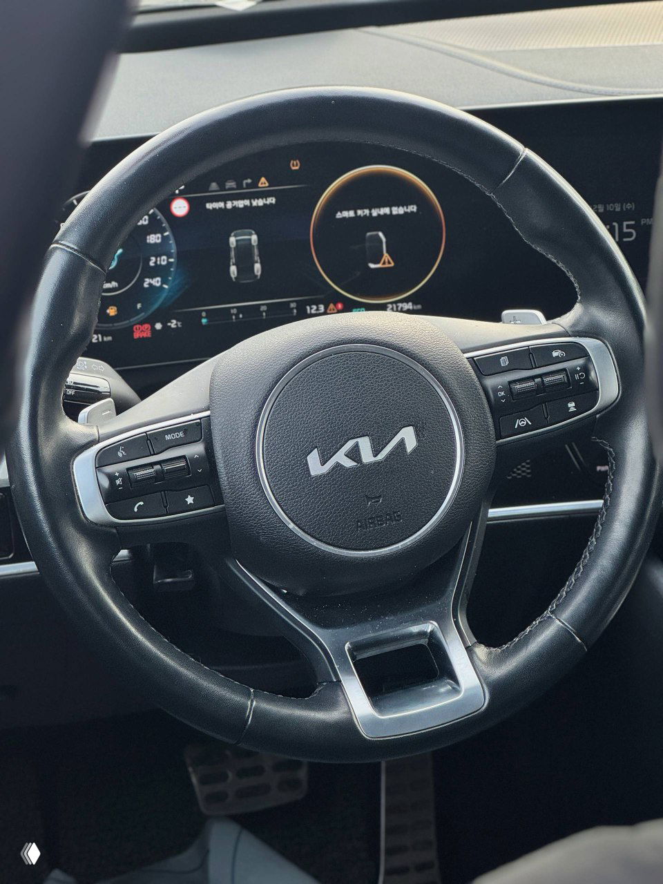 Рулевое колесо KIA с новым логотипом, панель приборов и цифровая приборная панель на фоне — вид оформления водительской зоны и кнопок на руле.