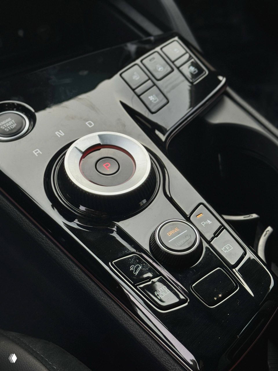 Крупный план селектора передач и кнопок управления режимами движения на глянцевой центральной площадке, видна кнопка P и селектор Drive вблизи.