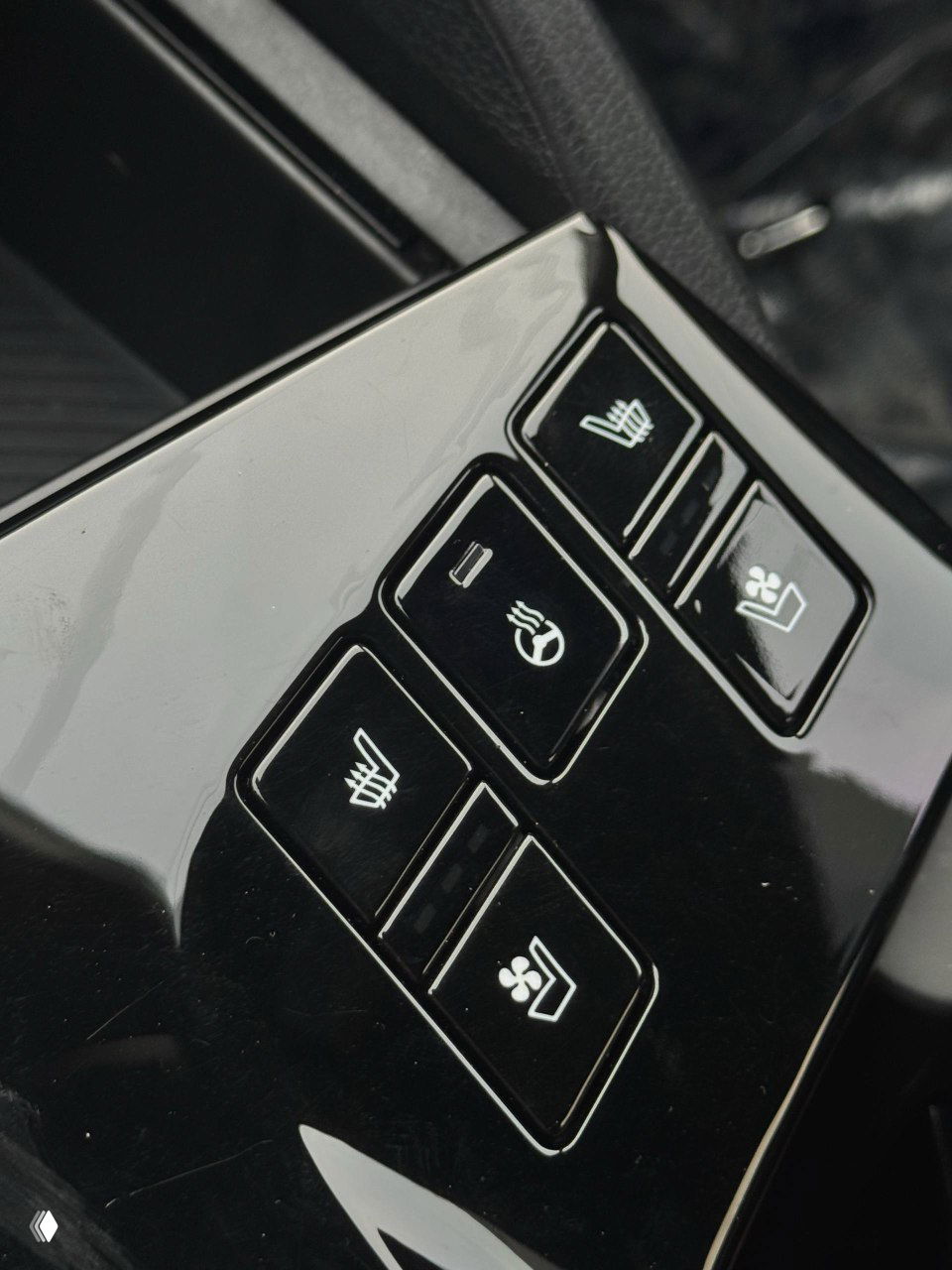 Крупный план кнопок обогрева и вентиляции сидений на панели, чёрная глянцевая отделка вокруг, акцент на опциях комфорта для передних сидений.