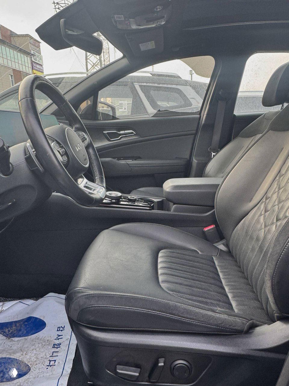 Вид на переднее пассажирское место и водительское сиденье KIA Sportage изнутри, чёрная кожа/тканевая отделка, панорамная крыша частично видна, общий интерьер.