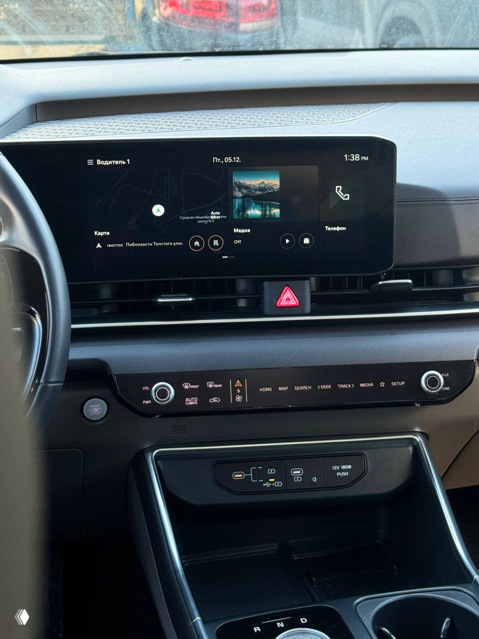 Центральный дисплей мультимедийной системы KIA Carnival с отображением карты и медиапанели, вид на консоль и вентиляционные решётки.