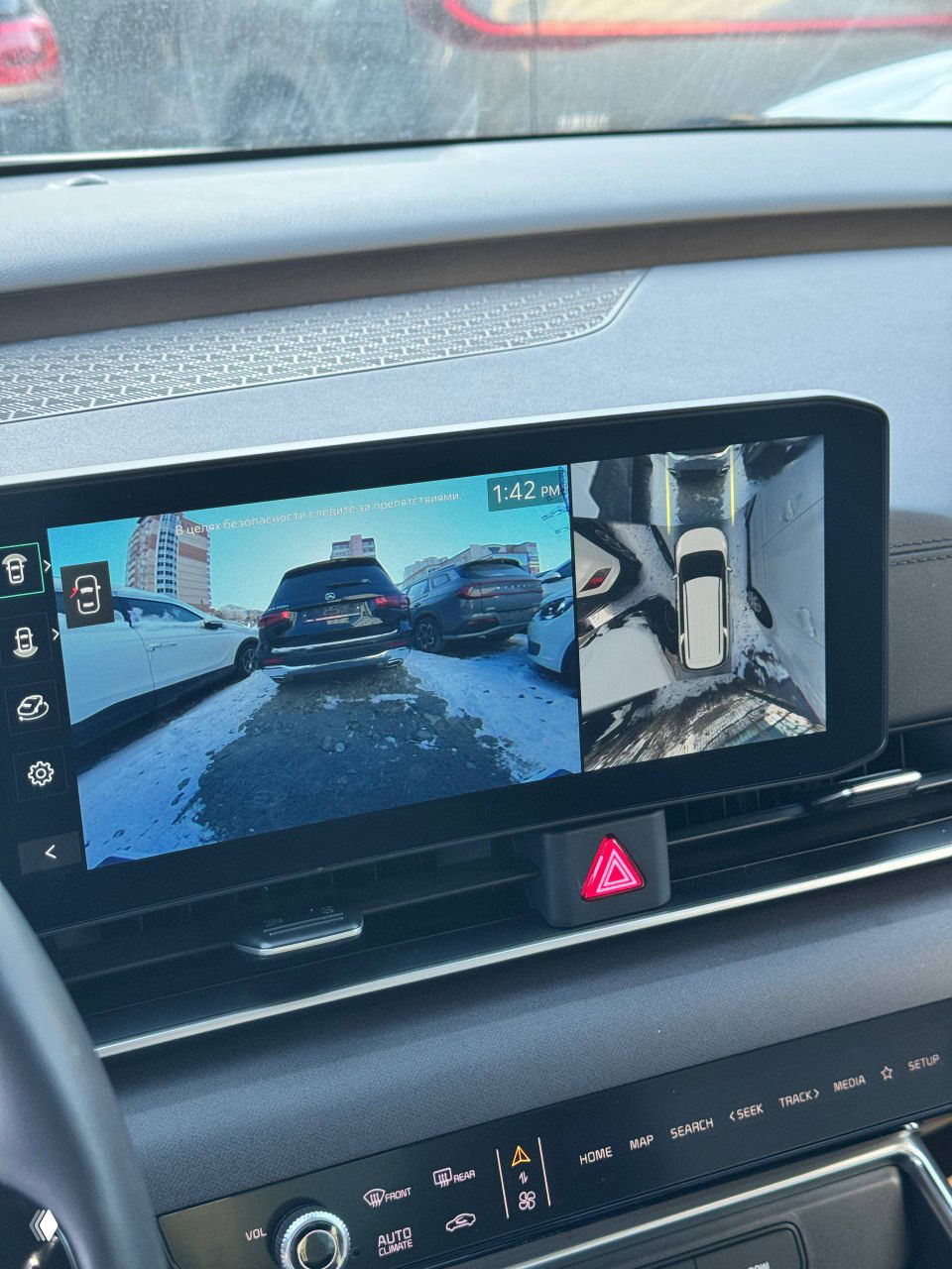 Широкий вид мультимедийного экрана с камерой заднего вида и панорамой сверху, интерфейс парковки на дисплее автомобиля.