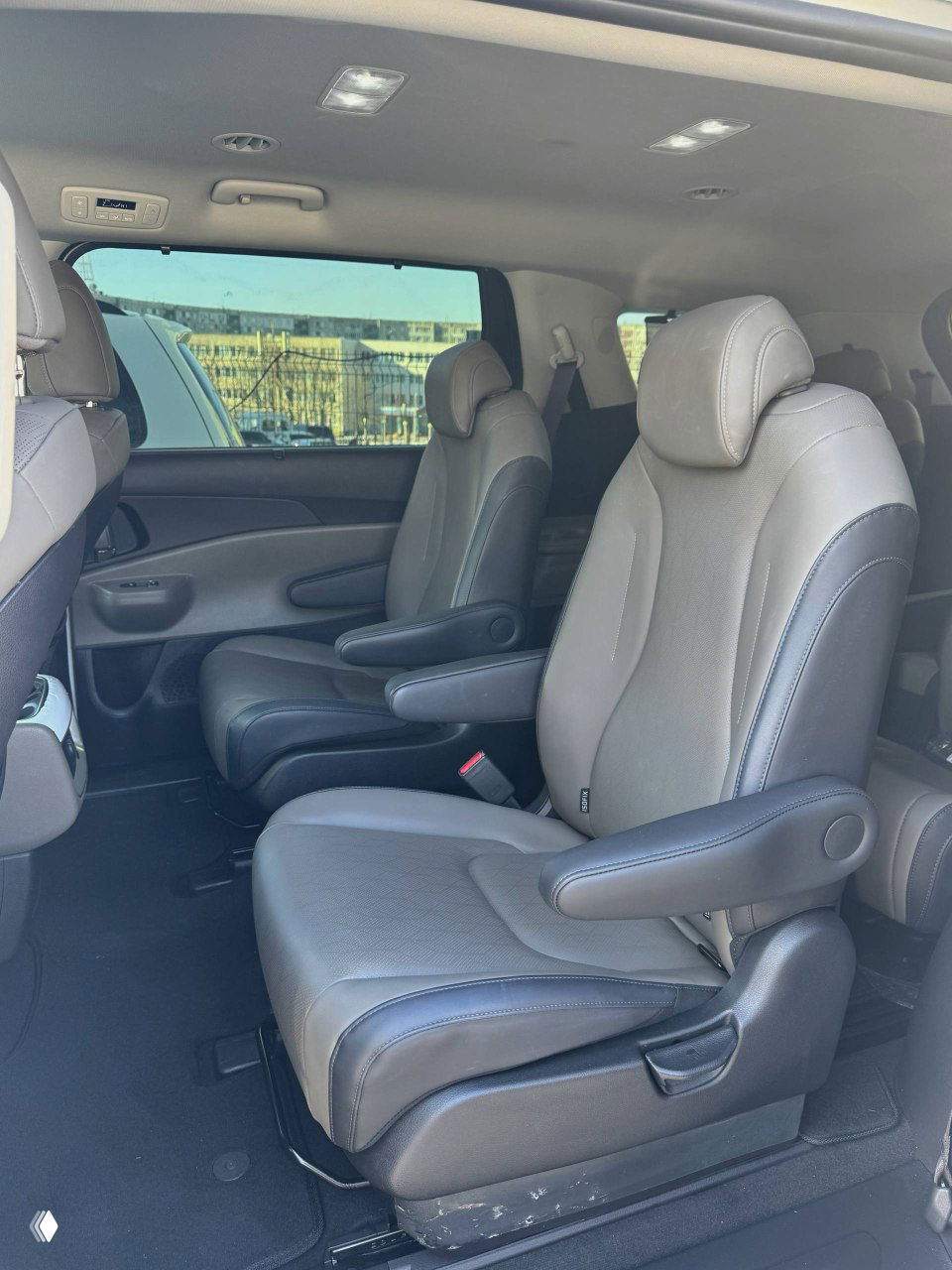 Второй ряд кресел KIA Carnival: два отдельных капитанских кресла с подлокотниками, обивка в серых тонах, чистый интерьер.