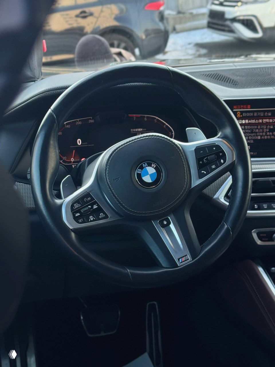 Салон: руль BMW M‑Sport с логотипом марки, крупный план приборной панели и мультируля в интерьере автомобиля с коричневой отделкой.