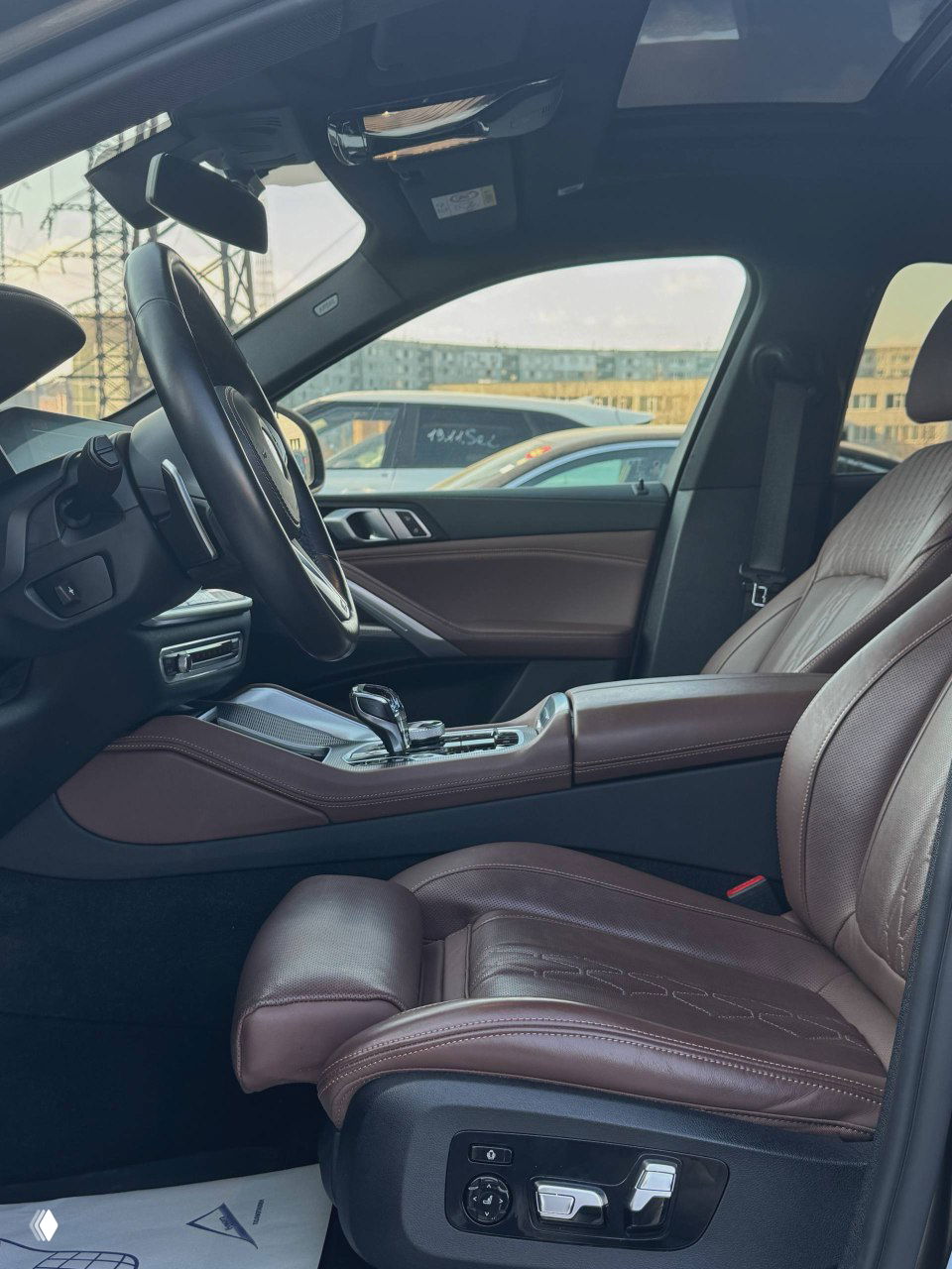 Вид на водительское место и переднее пассажирское кресло BMW X6: тёмно-коричневая кожаная отделка сидений, регулировки сиденья видны сбоку.