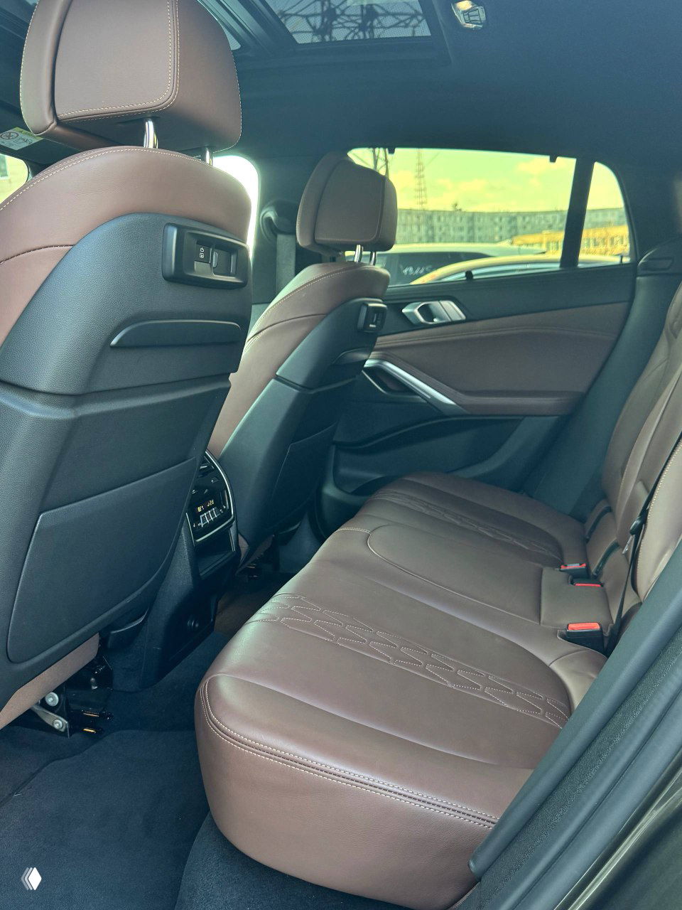 Задний ряд салона BMW X6: коричневые кожаные сиденья, достаточно места для пассажиров и вид на панель управления климатом для задних сидений.