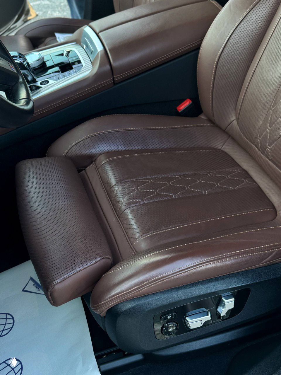 Крупный план переднего пассажирского кресла BMW X6: коричневая перфорированная кожа, удлинённая поддержка для ног и электроприводы регулировки.