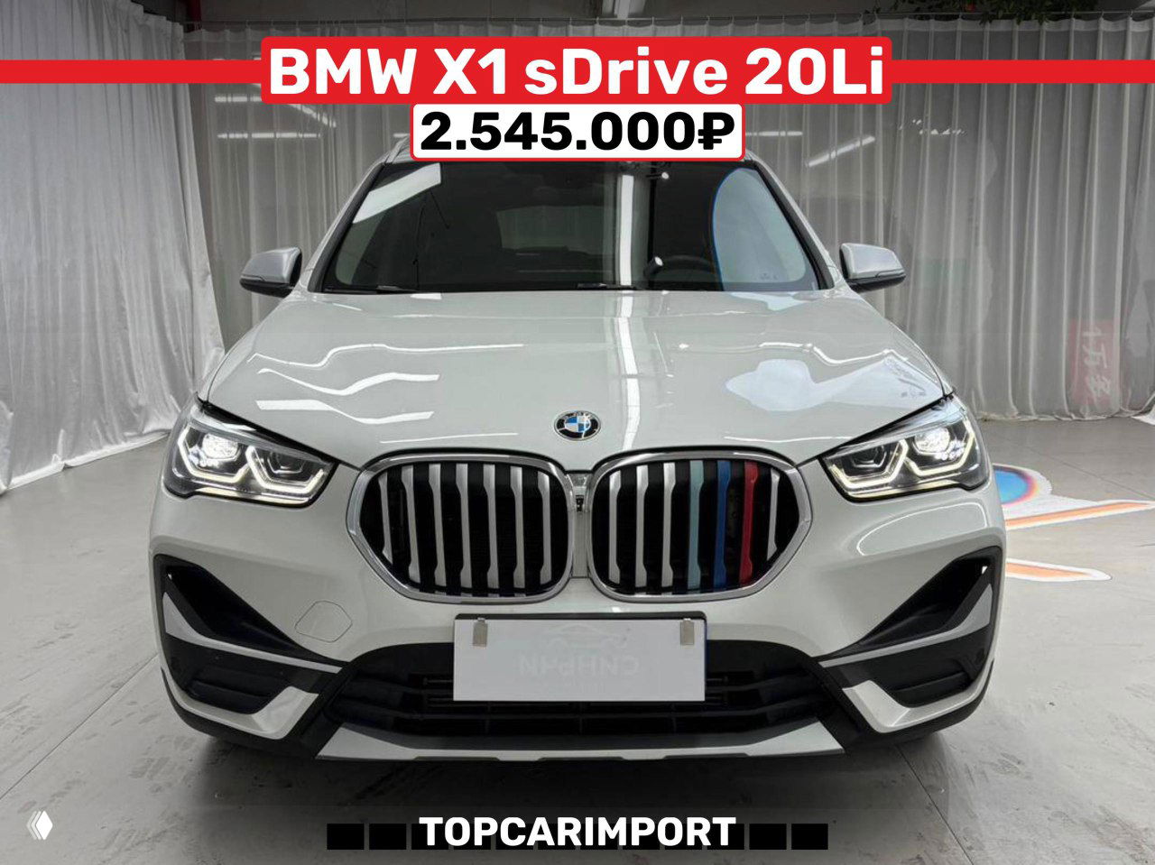 Крупный план белого BMW X1 sDrive 20Li в помещении, вид спереди с характерной радиаторной решёткой и ценой 2.545.000₽ на баннере.