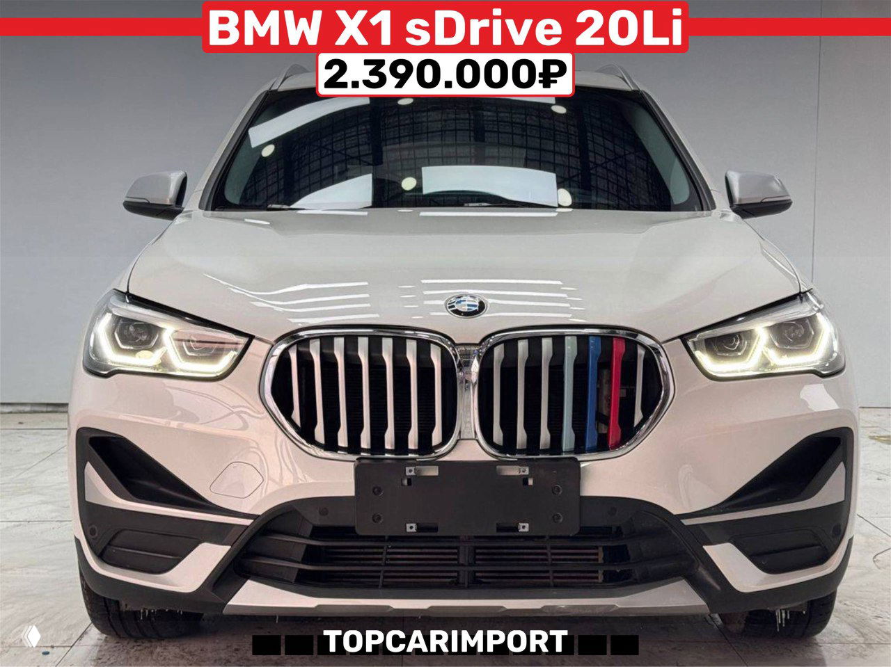 Фотография белого BMW X1 sDrive 20Li 2022 года в выставочном зале, фронтальный вид с логотипом и баннерной ценой 2.390.000₽ от TOPCARIMPORT.