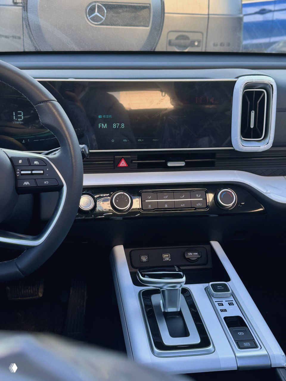 Мультимедийный экран и управляющие элементы на центральной консоли Hyundai Mufasa, отражение наружных объектов на стекле экрана заметно на фото.