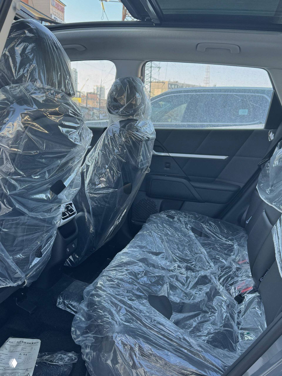 Задние сиденья Hyundai Mufasa, покрытые защитной плёнкой, видны подголовники, обшивка дверей и вентиляционные решётки для пассажиров сзади.