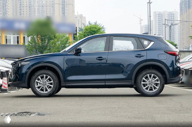 Боковой профиль Mazda CX-5 2025 тёмно-синего цвета на автостоянке в Китае, видна длина кузова на фоне городских зданий