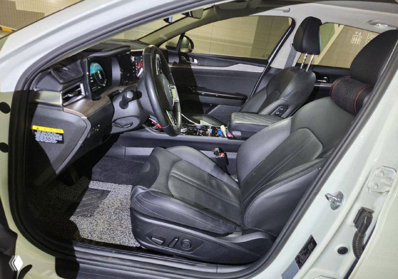 Интерьер KIA K5: вид водительского места и переднего пассажирского сиденья, чёрная кожаная отделка, панель приборов и рулевое колесо.