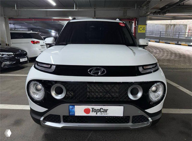 Фронтальный вид Hyundai Casper белого цвета на парковке, круглые дневные ходовые огни и характерная решётка радиатора, логотип TopCar на номере.