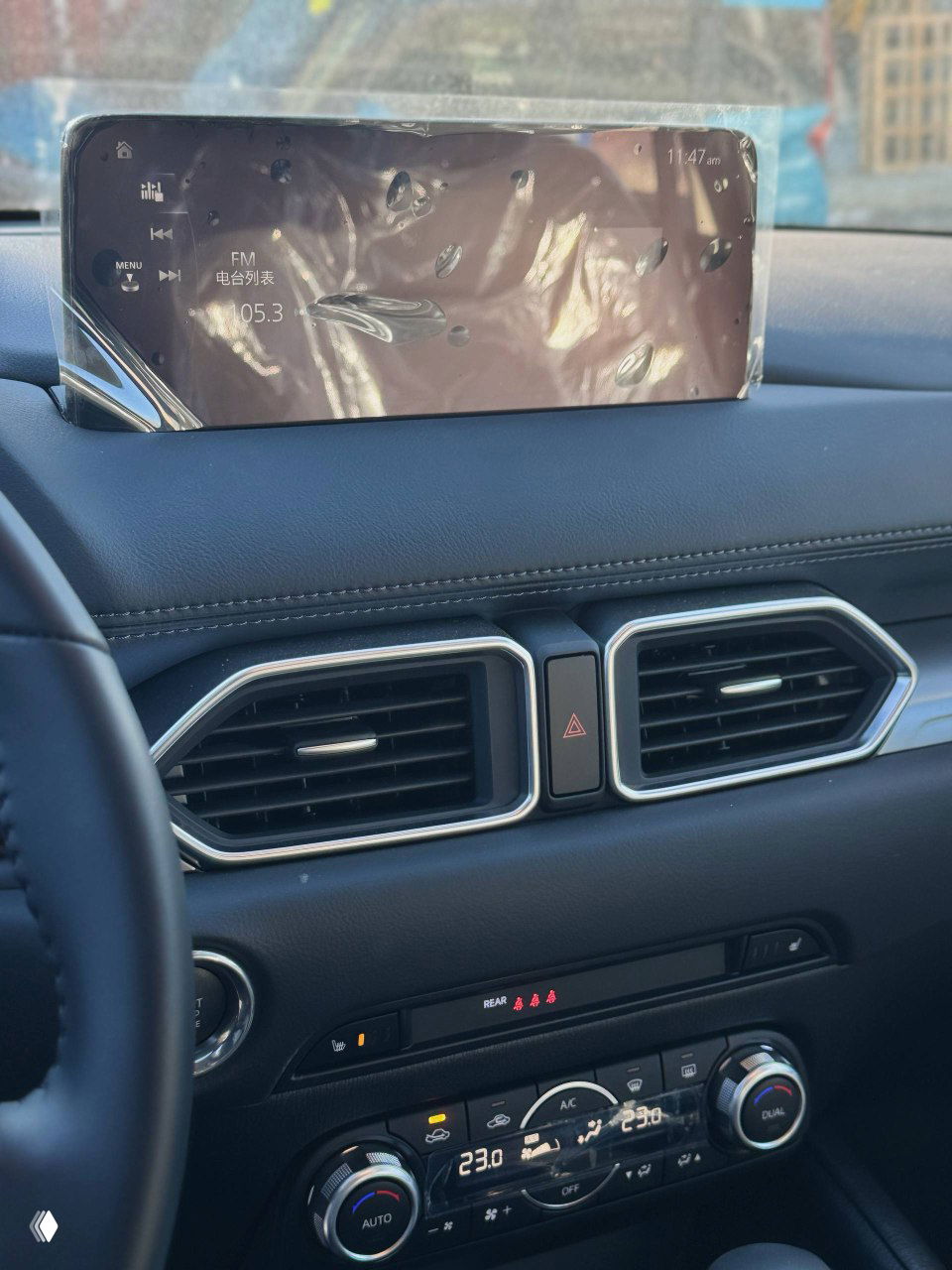 Дисплей мультимедийной системы Mazda на торпедо с защитной плёнкой; видны вентиляционные дефлекторы и часть управления климатом.