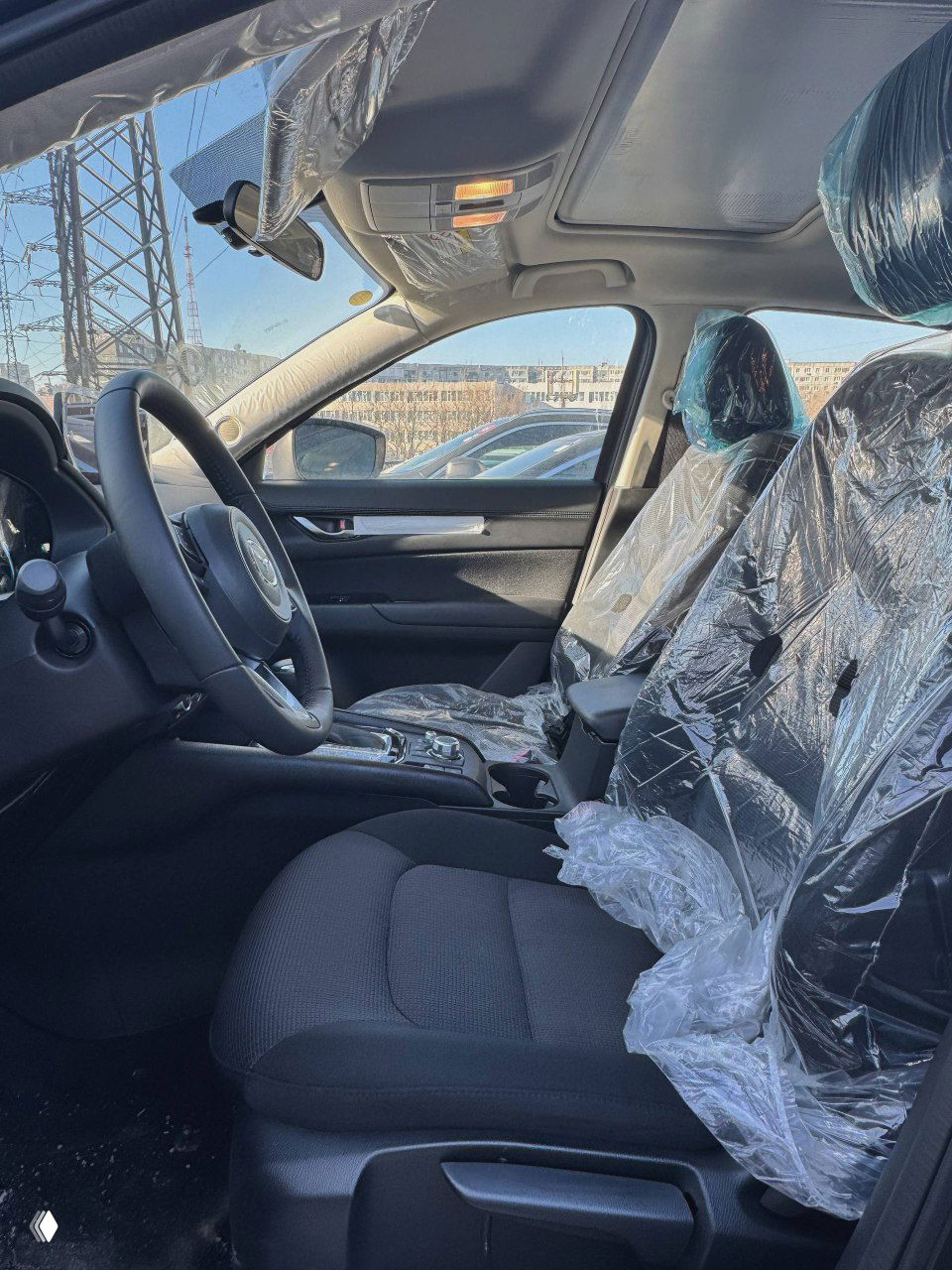 Вид спереди‑сбоку на пассажирские сиденья и панорамный обзор салона Mazda CX‑5 с заводской защитной плёнкой на креслах.