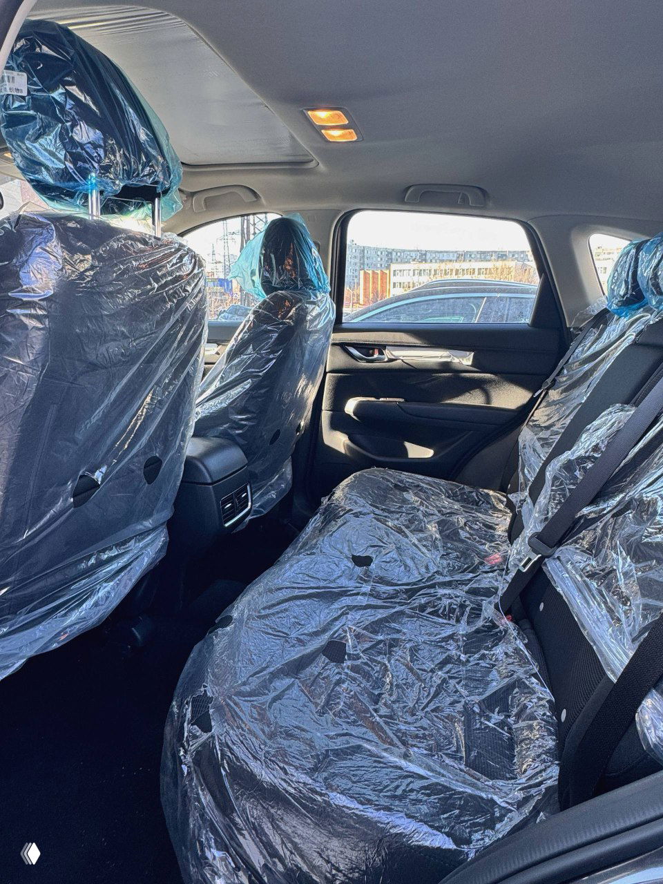 Вид на задний ряд сидений Mazda CX‑5, сиденья покрыты защитной плёнкой; видна достаточно просторная задняя пассажирская зона.