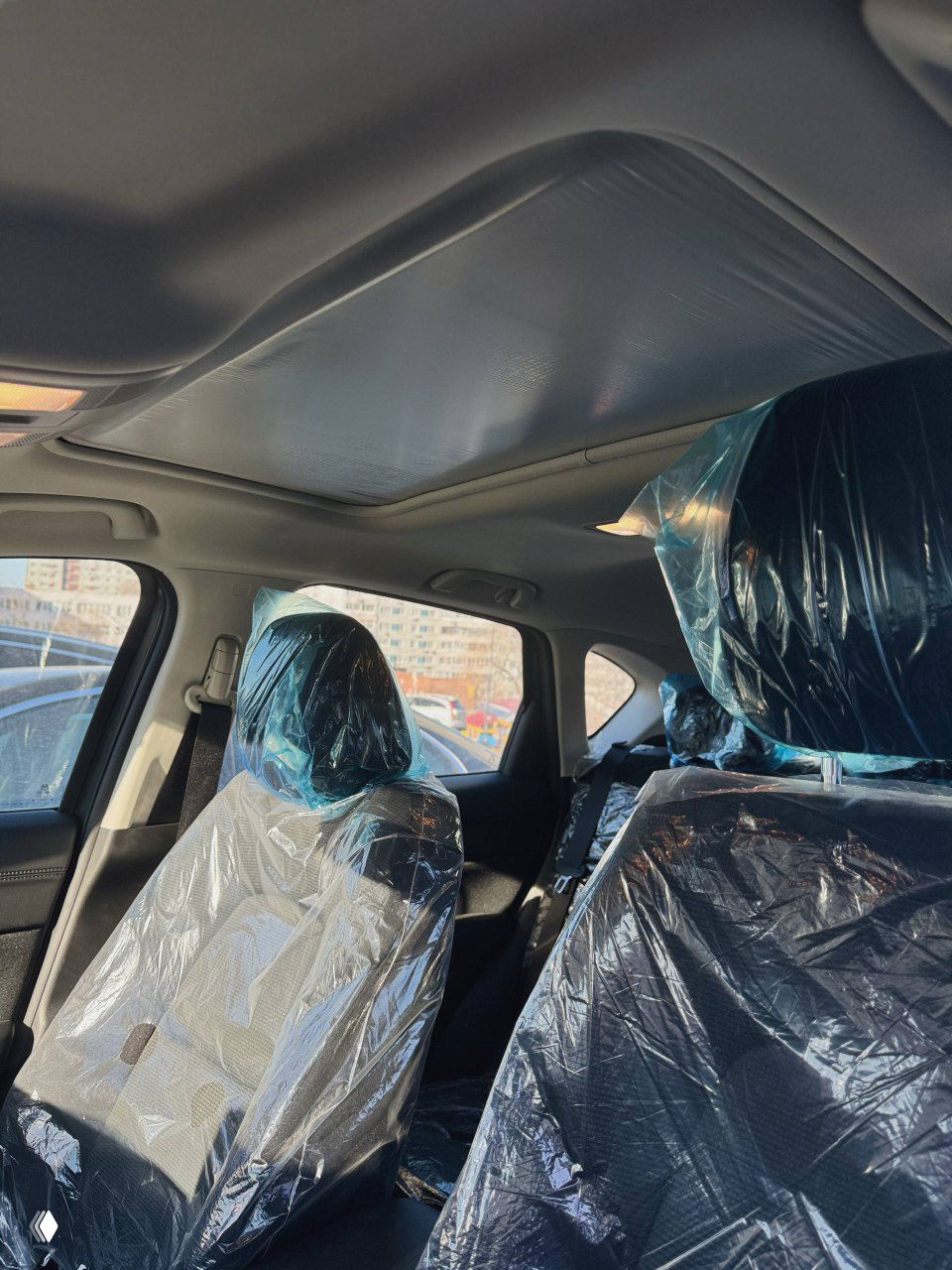 Вид вверх на потолок и люк Mazda CX‑5, передние сиденья в защитной плёнке; видно внутреннее освещение и обшивку крыши.