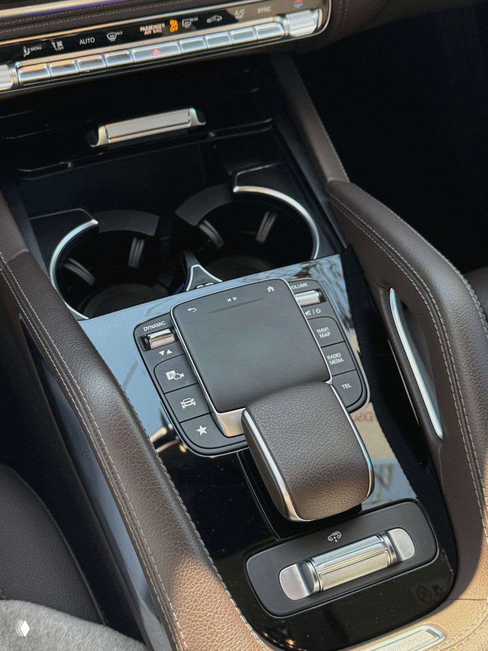 Крупный план центральной консоли Mercedes GLE300d: селектор передач, тачпад, элементы управления и подстаканники в коричневой отделке салона для проверки состояния.