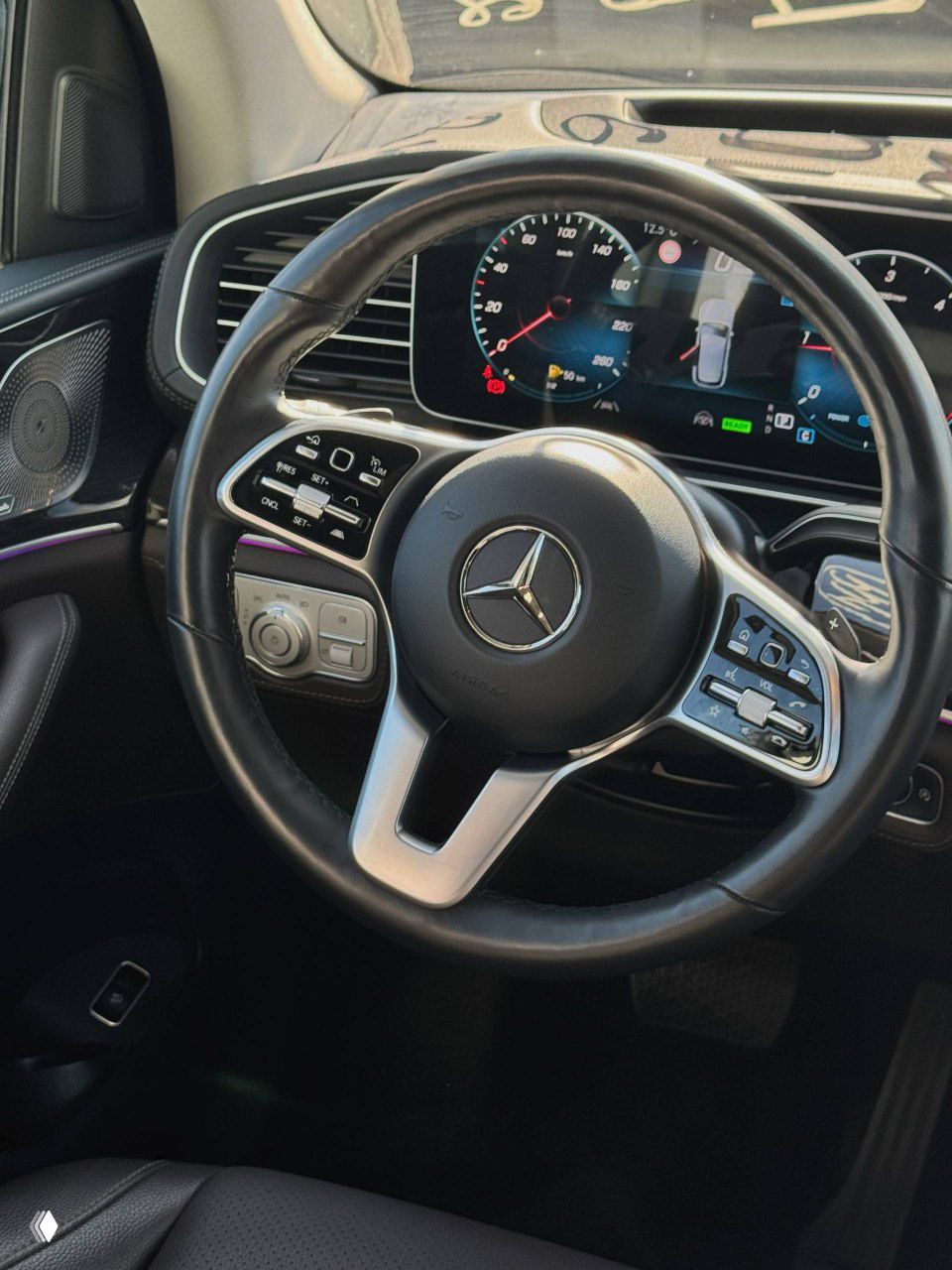 Руль Mercedes с логотипом и органами управления на крупном плане, видна приборная панель и элементы управления системой в салоне GLE300d.