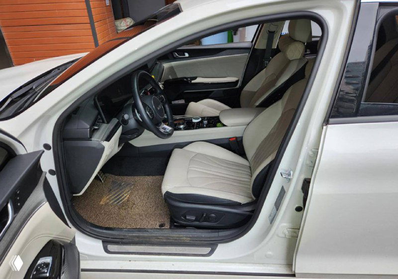 Салон автомобиля с бежёвой обивкой: передние сиденья, руль и приборная панель, открытая дверца и вид на водительское место.