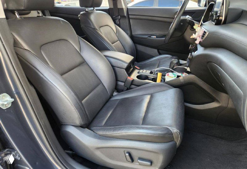 Салон Hyundai Tucson — чёрные передние кожаные сиденья, консоль и элементы управления, вид из открытой дверцы на водительское место.