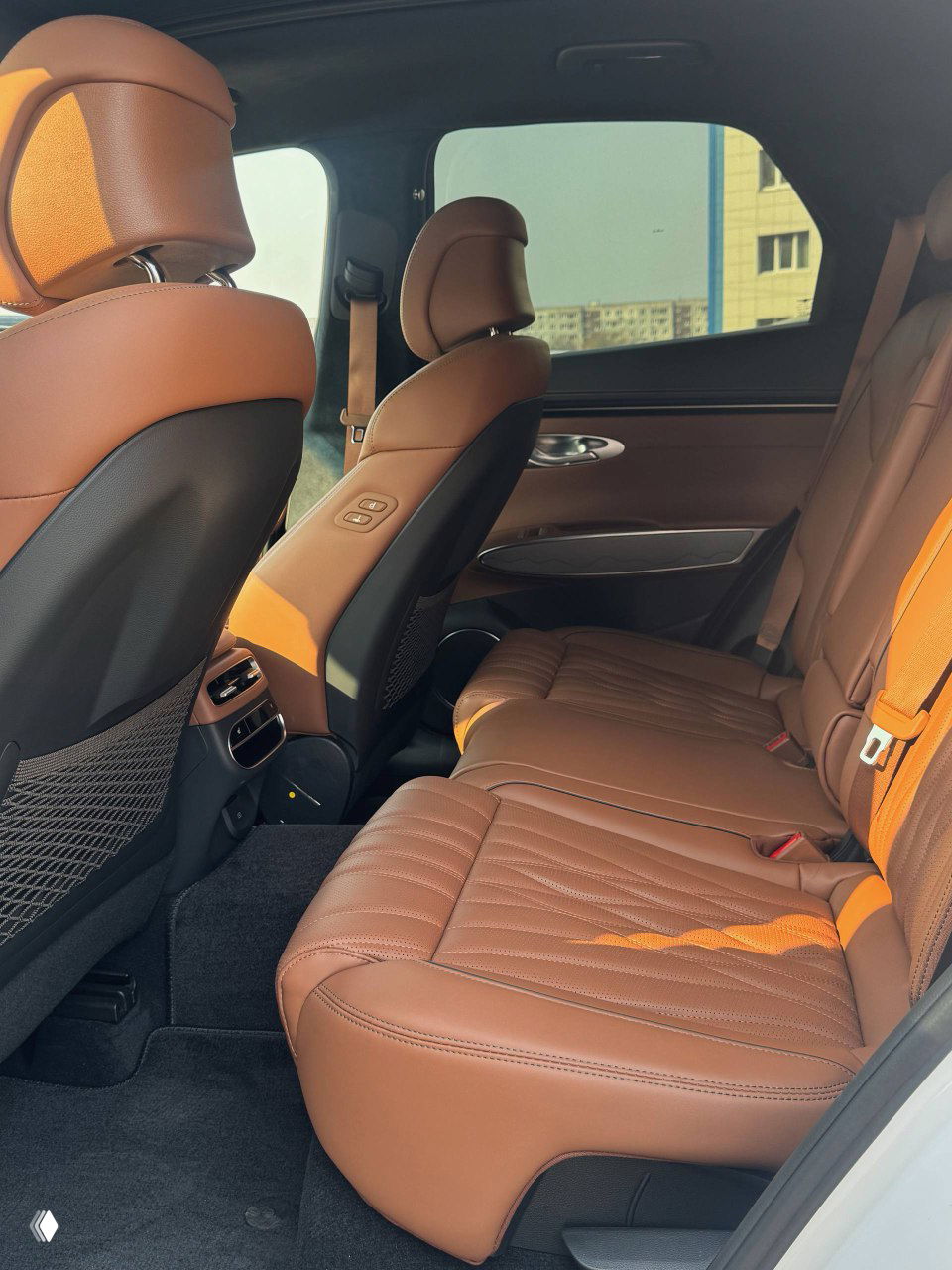 Водительское сиденье и руль Genesis GV70, коричневая кожа с прошивкой; видна центральная консоль и переднее кресло с регулировками на боковой панели.