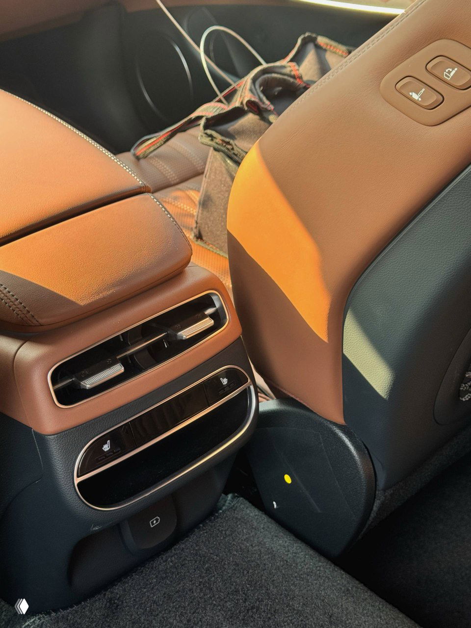 Задние сиденья Genesis GV70 в коричневой кожаной отделке, вид на пространство для ног и центральную консоль заднего ряда с вентиляционными решётками.